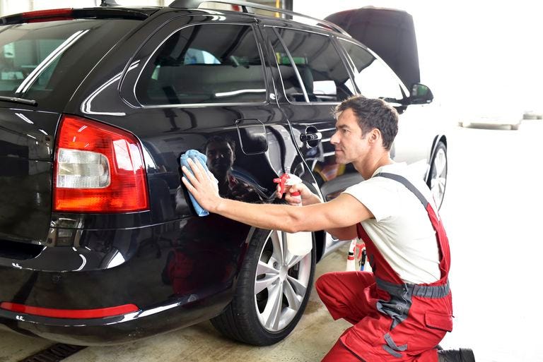 Technician working on surface prep beside a black vehicle